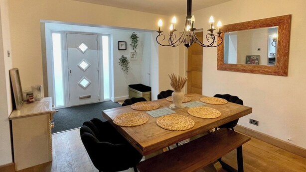A dining area with a wooden table, black chairs, a bench, a chandelier, and a mirror on the wall. - 4 Bedroom House, Sleeps 8- Hot Tub, Pets, Parking (Altrincham)