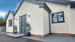 A modern two-story house with a grey exterior, a front door, and two windows. - 4 Bedroom House, Sleeps 8- Hot Tub, Pets, Parking (Altrincham)