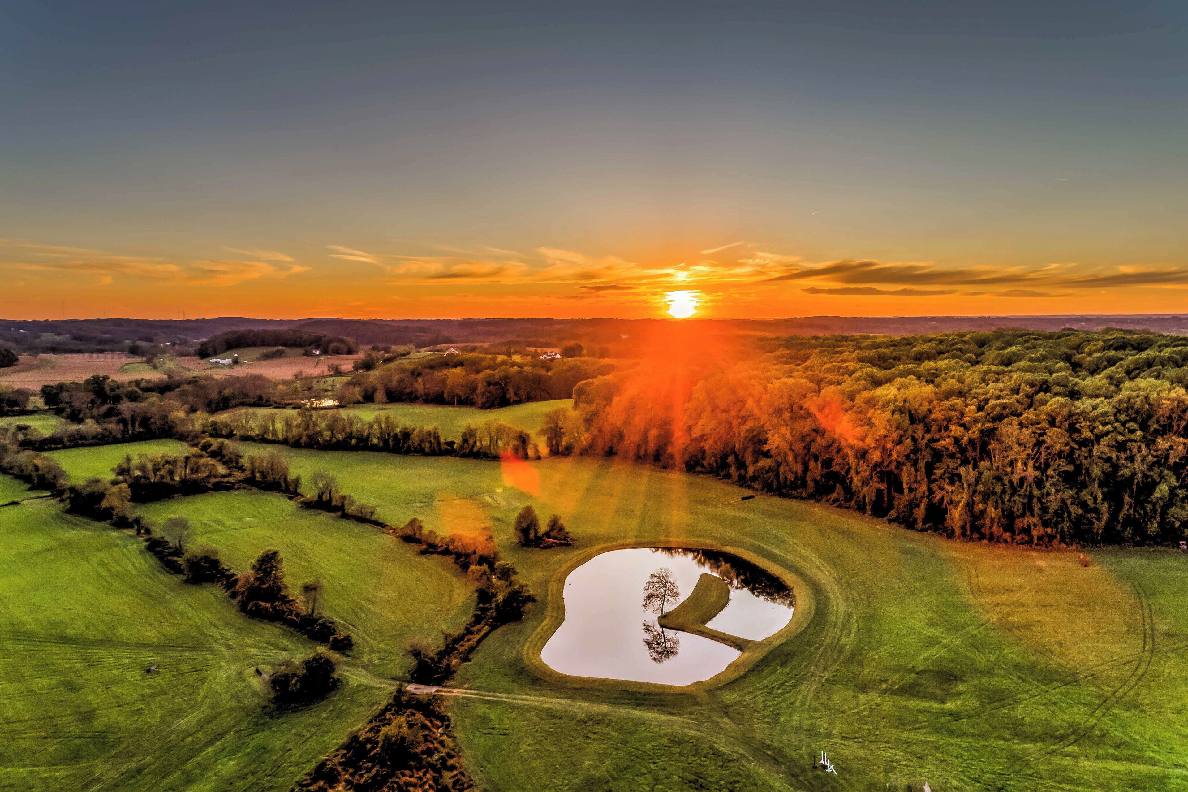 Ländliche Landschaft mit Teich, Feldern und Sonnenuntergang.