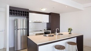 Une cuisine moderne avec un réfrigérateur en acier inoxydable, des armoires blanches, un évier à deux bacs et deux tabourets.