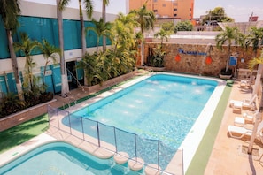 Ein Pool mit Steinmauer, Palmen und Liegestühlen.