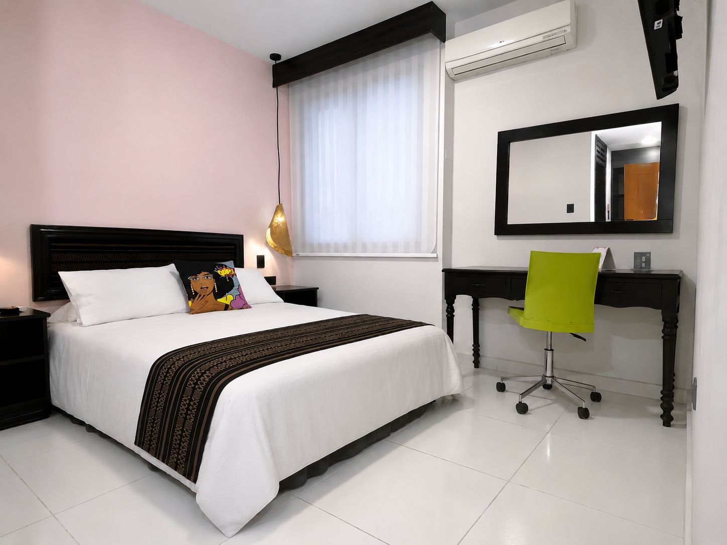Una habitación de hotel con cama, mesita de noche, silla, escritorio y un espejo grande.