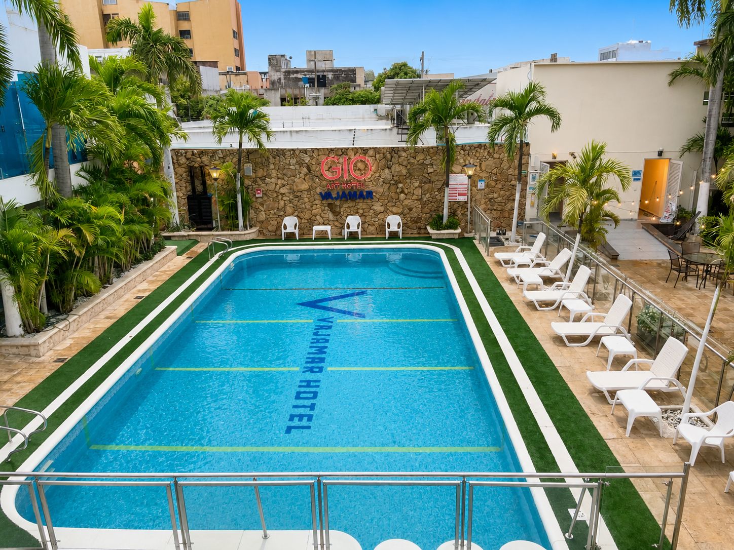 Una piscina con la inscripción 'Vajama Hotel' reflejada en el agua, rodeada de tumbonas y palmeras.
