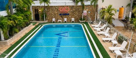 Una piscina con la inscripción 'Vajama Hotel' reflejada en el agua, rodeada de tumbonas y palmeras.
