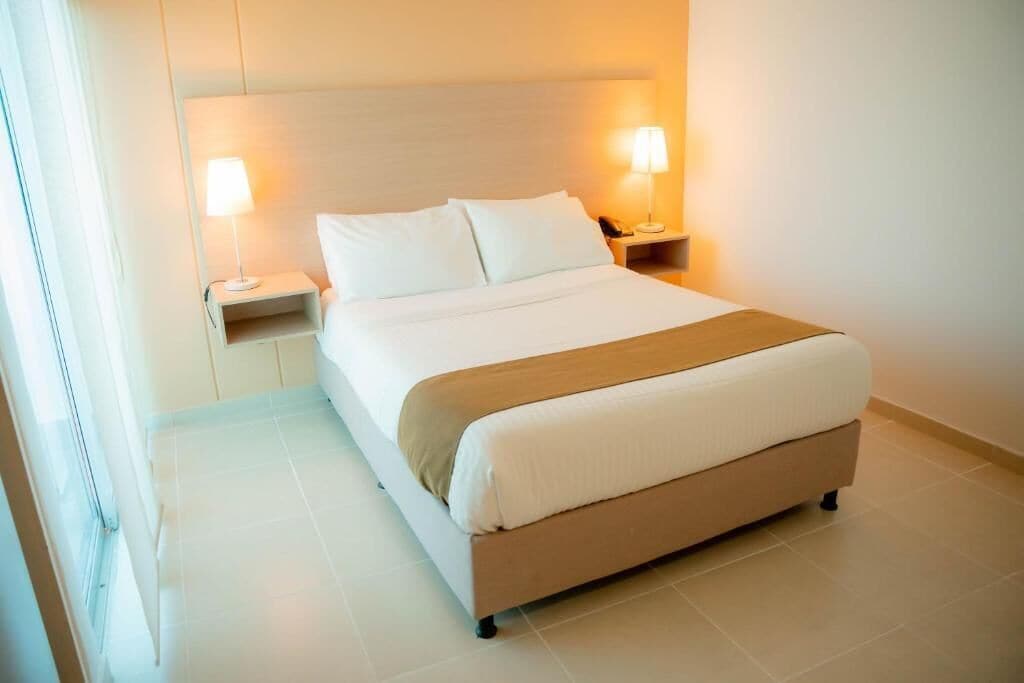 A neatly made bed with white linens and a brown throw, flanked by two bedside lamps on matching nightstands.