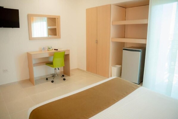Une chambre à coucher comprenant un lit, un bureau avec une chaise, une armoire, un téléviseur et un réfrigérateur.