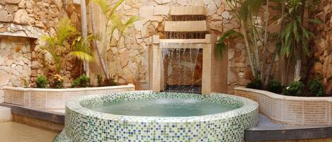 A hot tub with a mosaic tile design, surrounded by a stone wall and palm trees.