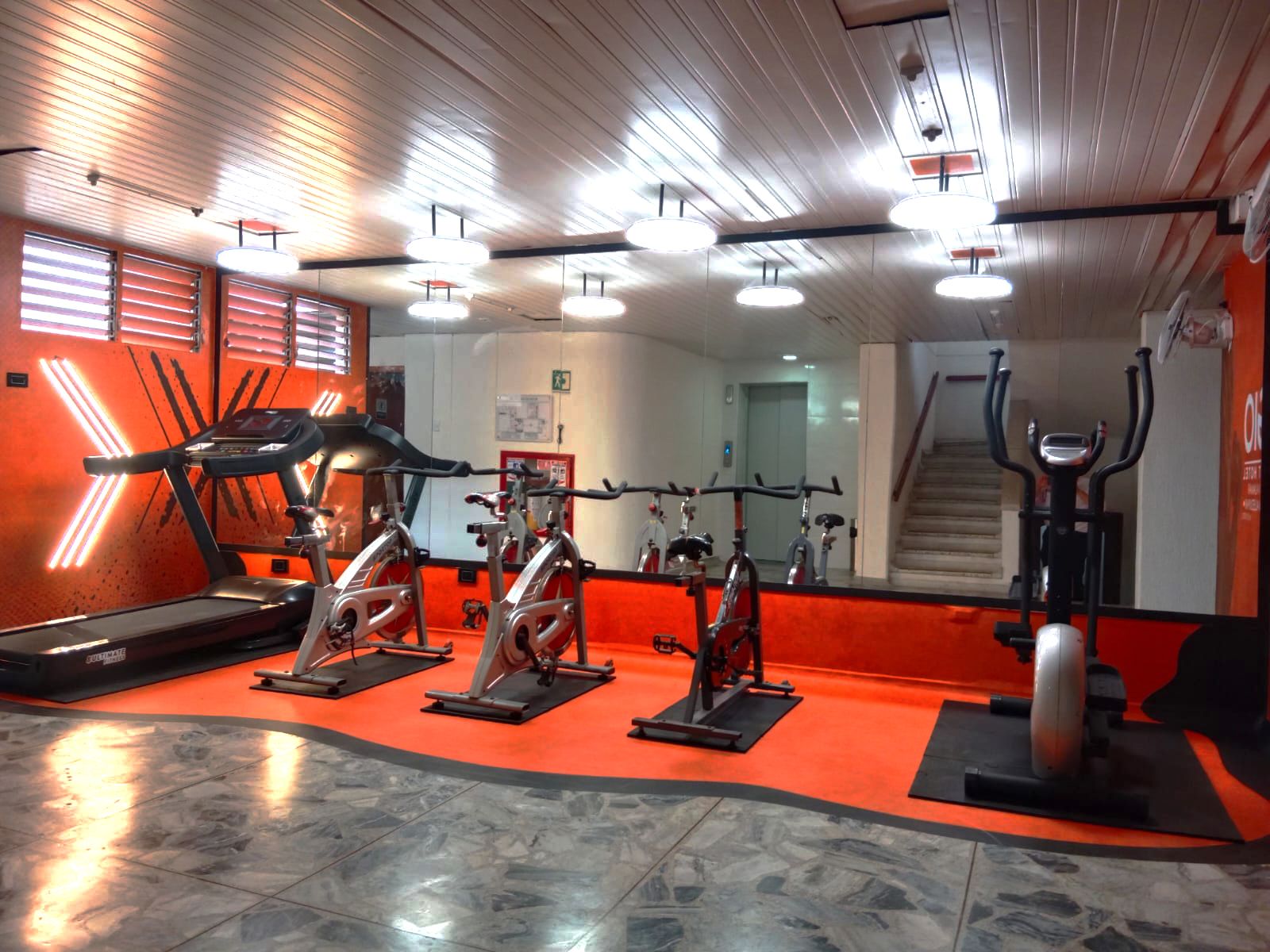 A gym with exercise equipment, a mirrored wall, and a staircase.