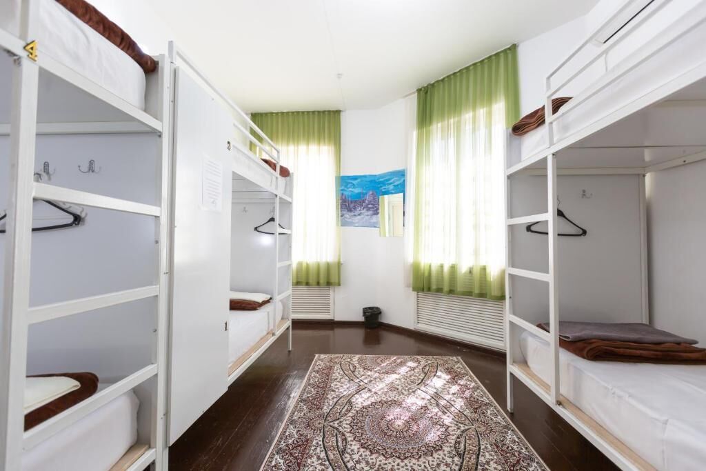 A dormitory room with bunk beds, a patterned rug, and a painting of a snowy landscape.
