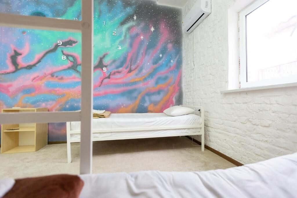 A bedroom with a bunk bed, a white brick wall, a window, and a galaxy-themed mural on the wall.