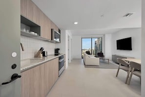 A modern kitchen with a built-in microwave, a dining area with a table and chairs, and a large window offering a city view.