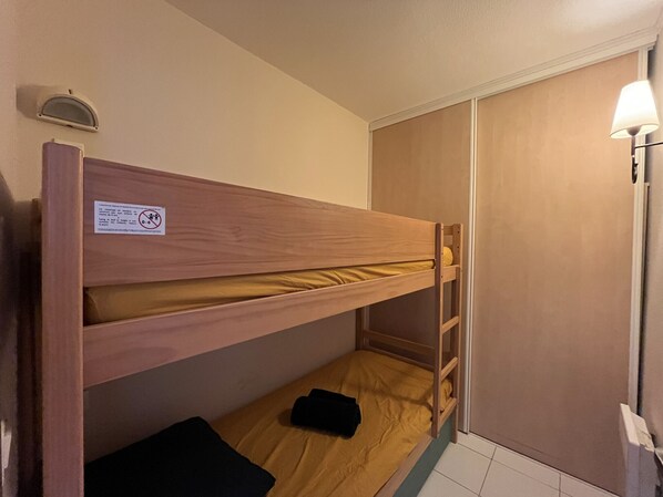 Een slaapkamer met stapelbed, een houten hoofdbord, een klein plankje en een wandlamp.