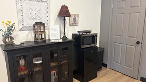 A kitchen with a black cabinet, a microwave, and a small refrigerator. There is a framed picture on the wall and a vase with flowers on the cabinet.