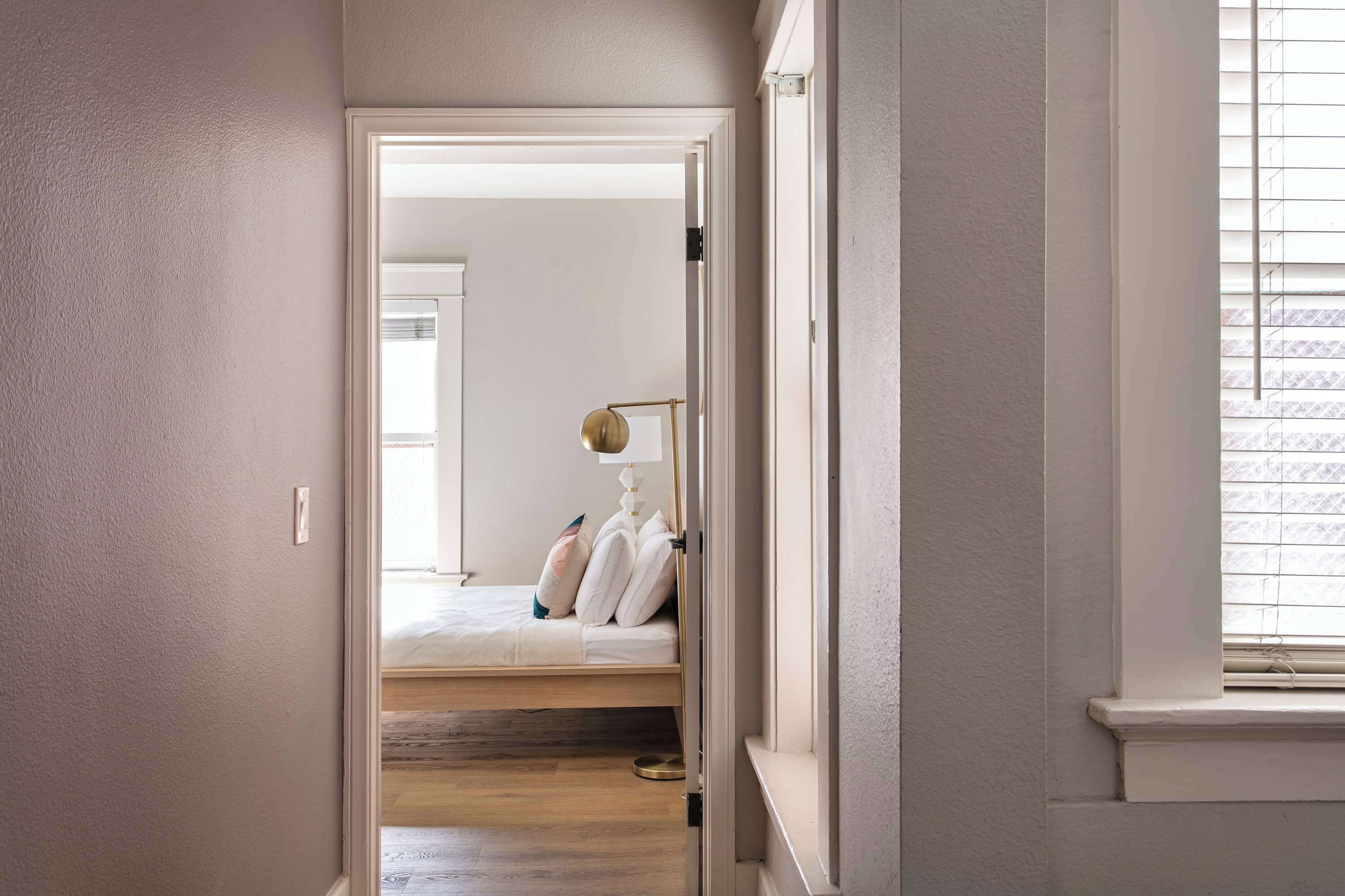 A hallway leading to a bedroom with a bed, pillows, and a lamp.