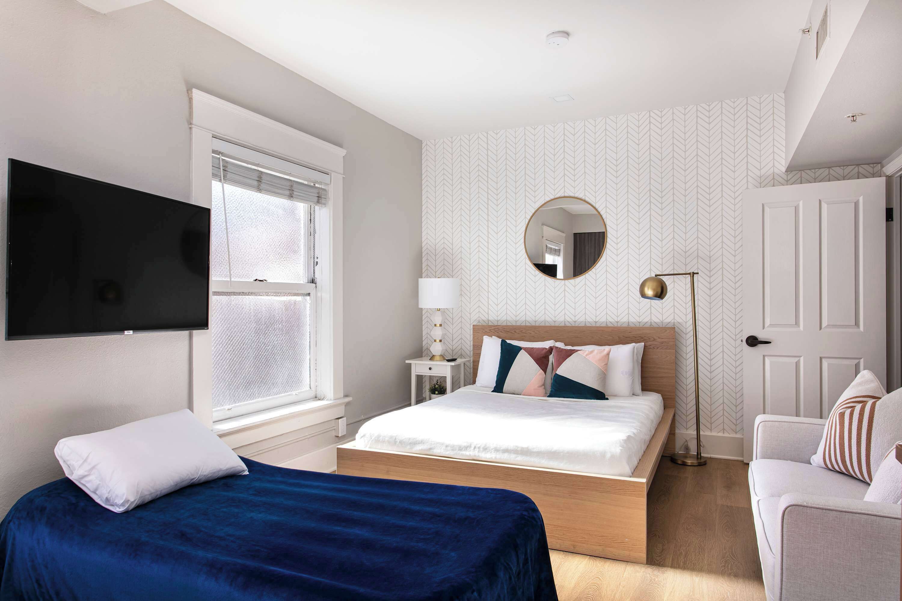 A bedroom with a bed, a TV, a bedside table, a lamp, and a chair.