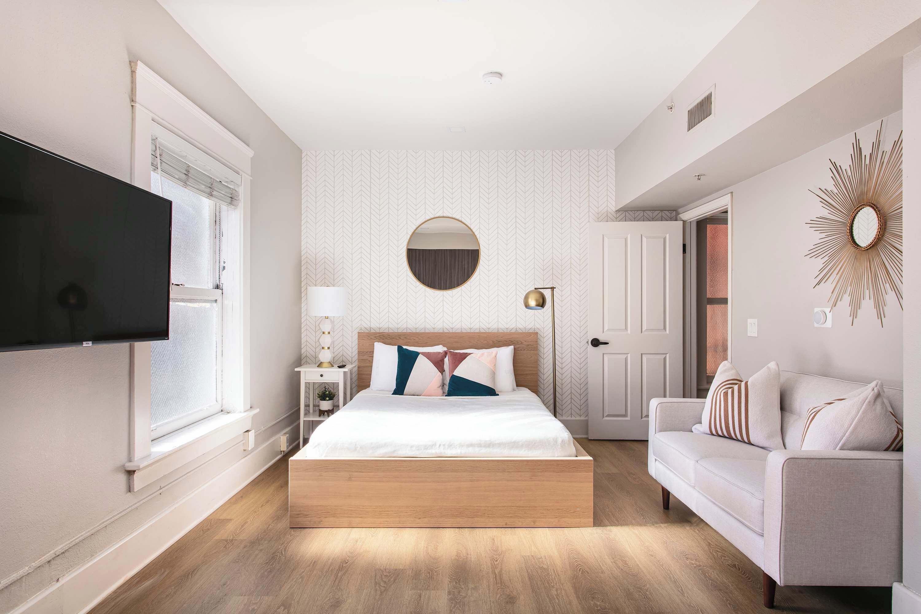 A modern bedroom with a large bed, a TV, a sofa, and a decorative mirror.