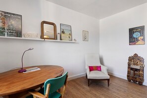 Una habitación con una mesa de comedor de madera, sillas, un sillón blanco, un espejo y una obra de arte en la pared.