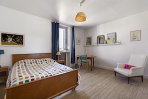 Un dormitorio con cama de madera, una silla, una mesita y una ventana con cortinas.