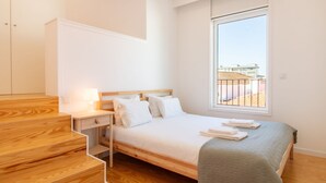 Un dormitorio con cama, mesita de noche, lámpara, ventana con vistas y una escalera de madera.