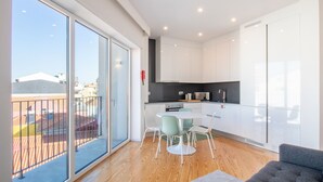 Un apartamento moderno con balcón, cocina con armarios blancos, comedor con mesa y sillas, y sofá gris.