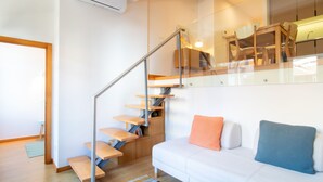 A modern living room with a staircase, a white sofa, and a glass railing. - Bright 1BR w/ Parking in Bolhão by LovelyStay (Porto)