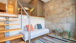 A modern interior with a staircase, a white sofa with colorful cushions, and a stone wall. - Bright 1BR w/ Parking in Bolhão by LovelyStay (Porto)