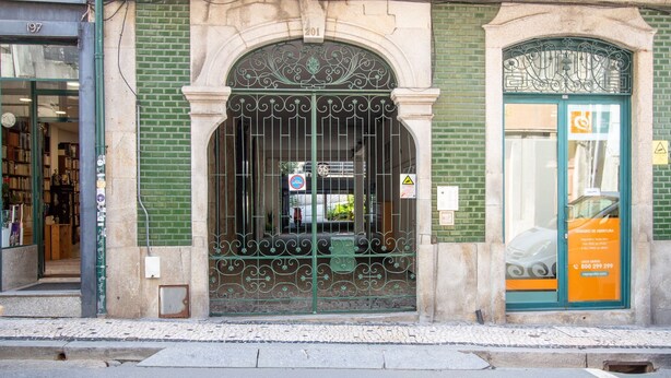 A building with a green brick facade, a metal gate with decorative patterns, and a door with a sign indicating a business. - Bright 1BR w/ Parking in Bolhão by LovelyStay (Porto)