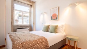 A bedroom with a bed, a window, a radiator, a bedside table, and a wall-mounted light fixture. - Bright 1BR w/ Parking in Bolhão by LovelyStay (Porto)