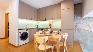 A compact kitchen with a washing machine, a dining table with chairs, and a stone wall. - Bright 1BR w/ Parking in Bolhão by LovelyStay (Porto)