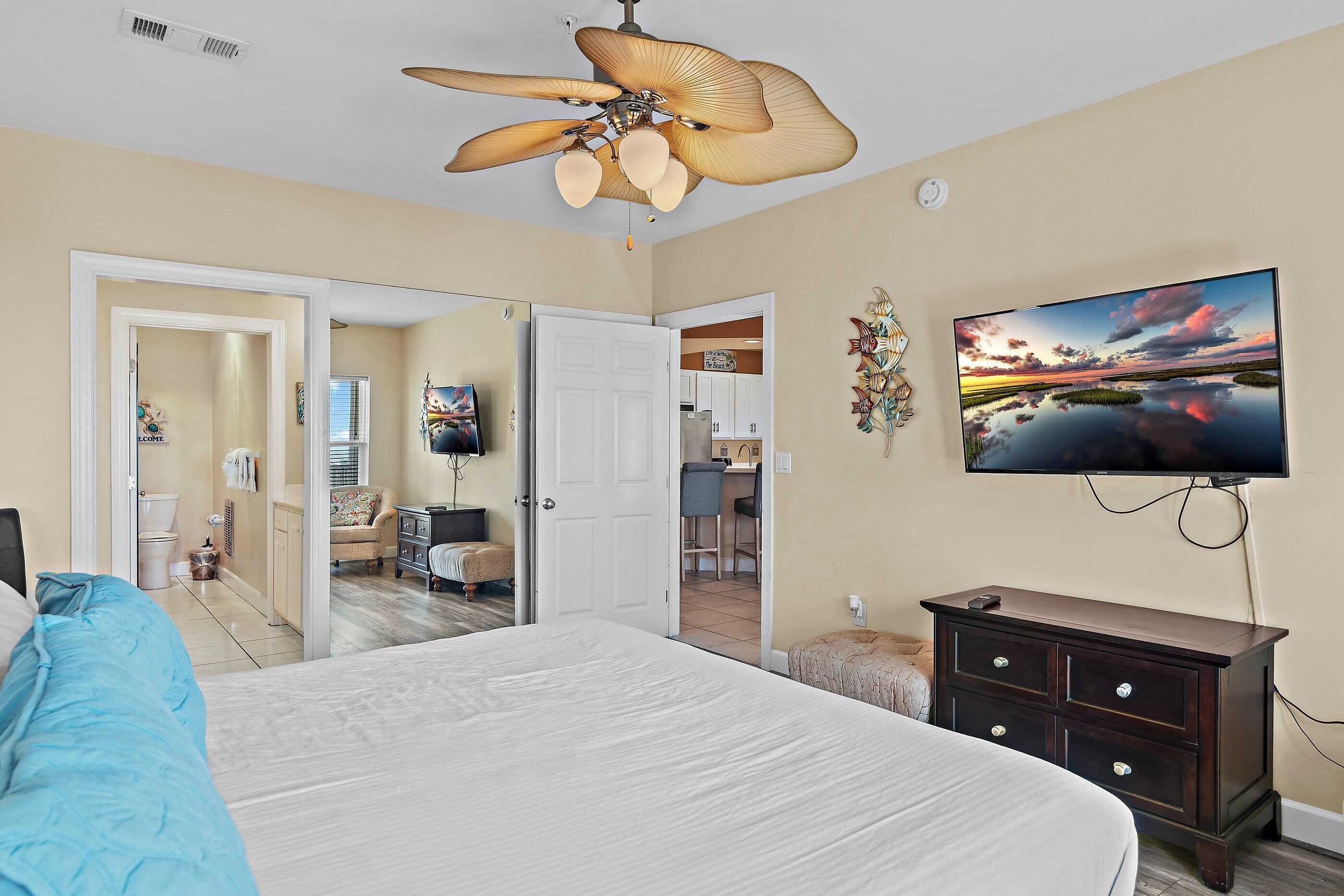 A bedroom with a bed, a ceiling fan, a television, and a dresser.