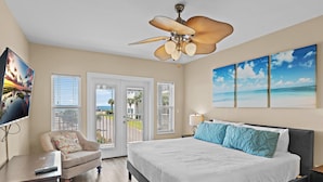 A bedroom with a bed, a chair, a ceiling fan, and a view of the outdoors. - Pavilion Palms 105c- The Emerald Jewel (Miramar Beach)
