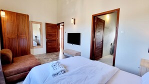 A bedroom with a bed, a chair, a TV, and a wooden wardrobe. - Royal Residence A3 - Gated Semi Detached Spacious Residence in Pereybere (Grand Baie)