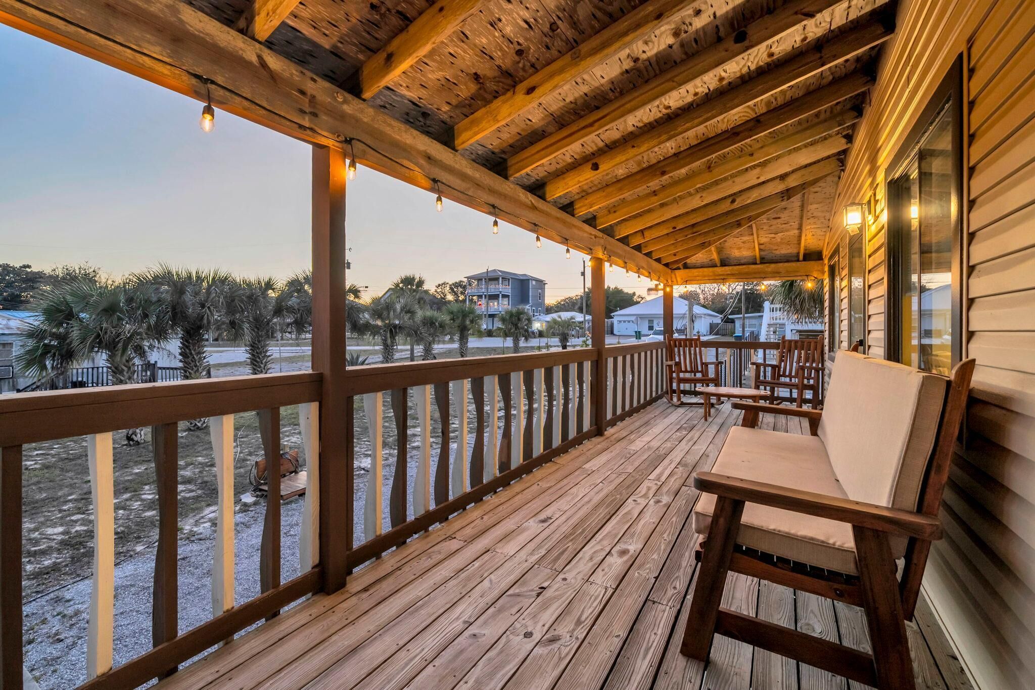 A wooden deck with a railing, a cushioned bench, and a view of palm trees and buildings in the distance.