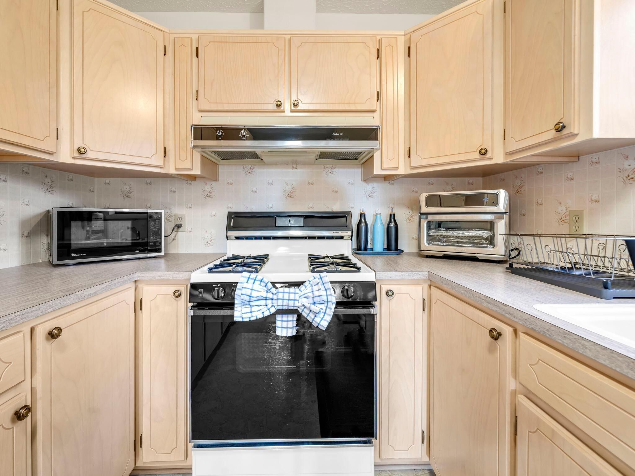 A kitchen with light wooden cabinets, a stove, a microwave, and a toaster.