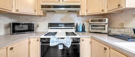 A kitchen with light wooden cabinets, a stove, a microwave, and a toaster.