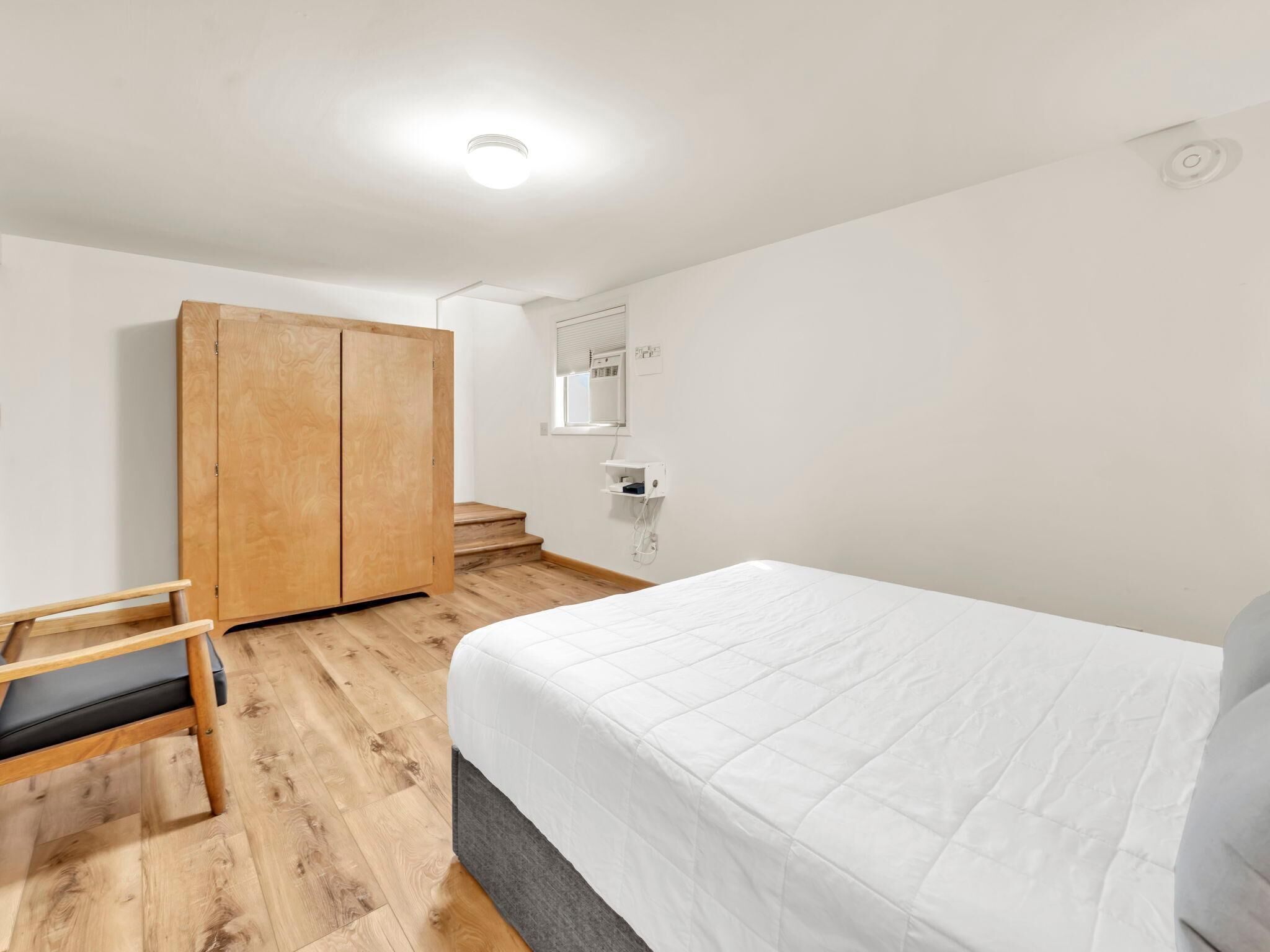 A bedroom with a bed, wooden wardrobe, and a chair.