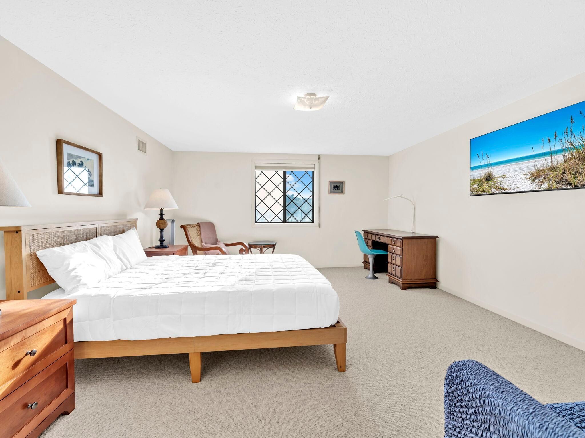 A bedroom with a bed, a desk, a chair, a dresser, a lamp, a window, and a painting.