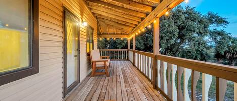A wooden deck with a round table and chairs, a railing, and string lights.