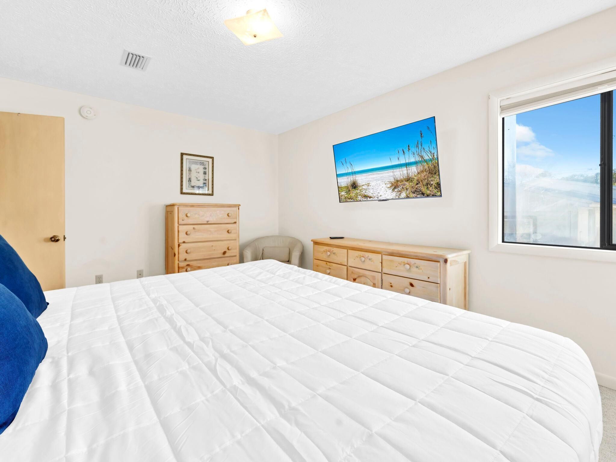 A bedroom with a bed, a dresser, a chair, a picture on the wall, and a window.