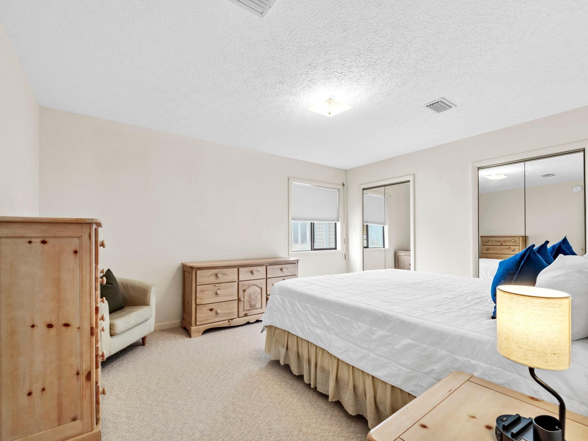 A bedroom with a bed, a dresser, a mirror, and a lamp.
