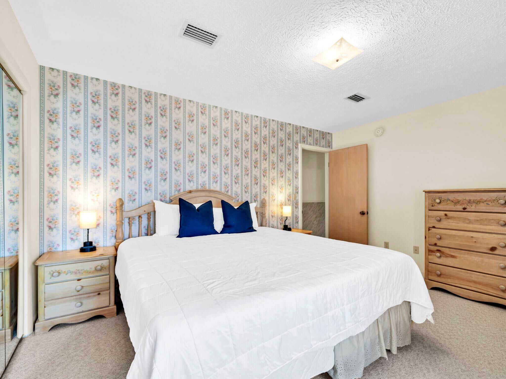 A bedroom with a bed, nightstands, a dresser, and floral wallpaper.
