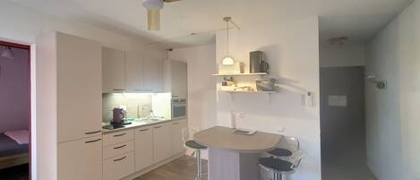 A compact kitchen with a central island, a ceiling fan, and a small bar stool.