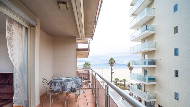 A balcony with a table and chairs, overlooking a beach and a high-rise building.