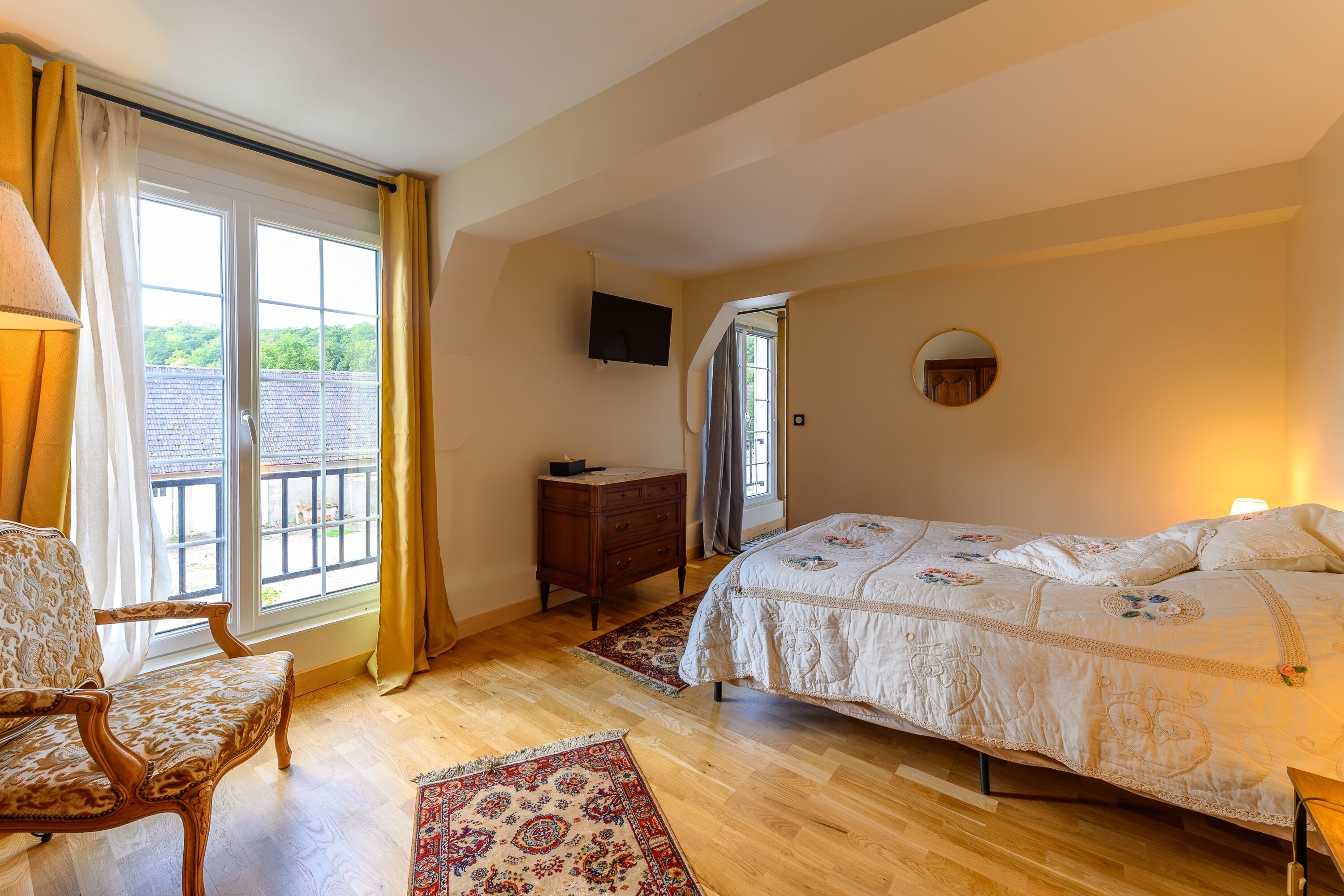 A bedroom with a bed, a chair, a dresser, a TV, and a window with curtains.