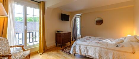 A bedroom with a bed, a chair, a dresser, a TV, and a window with curtains.