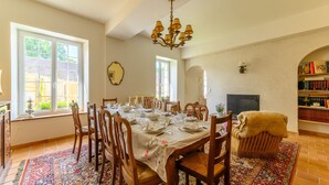 Comedor con una mesa grande dispuesta para seis comensales, rodeada de sillas de madera, un tapete estampado y una lámpara de araña.
