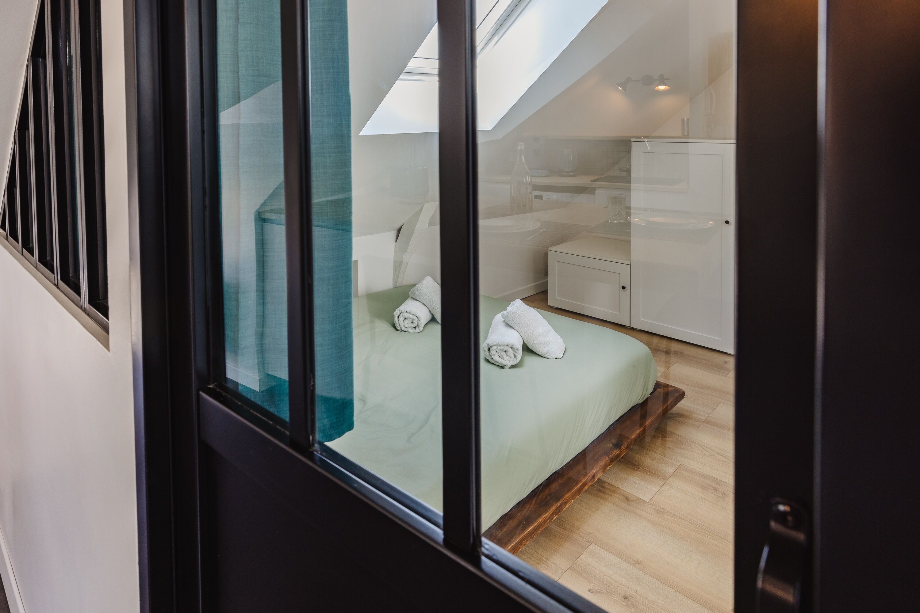 Un dormitorio moderno con tragaluz, una cama con toallas enrolladas, una mesita de noche y un pequeño armario blanco.