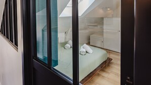 A modern bedroom with a skylight, a bed with rolled towels, a bedside table, and a small white cabinet. - Le Cosy Comble - 10 min Campus Kerlann (Bruz)