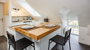 A modern kitchen with a wooden island, two black chairs, and a skylight. - Le Cosy Comble - 10 min Campus Kerlann (Bruz)