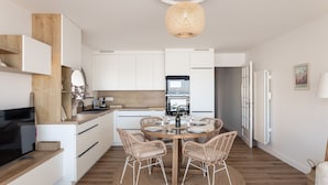 Una cocina moderna con armarios blancos, una zona de comedor con sillas de mimbre y una mesa redonda.